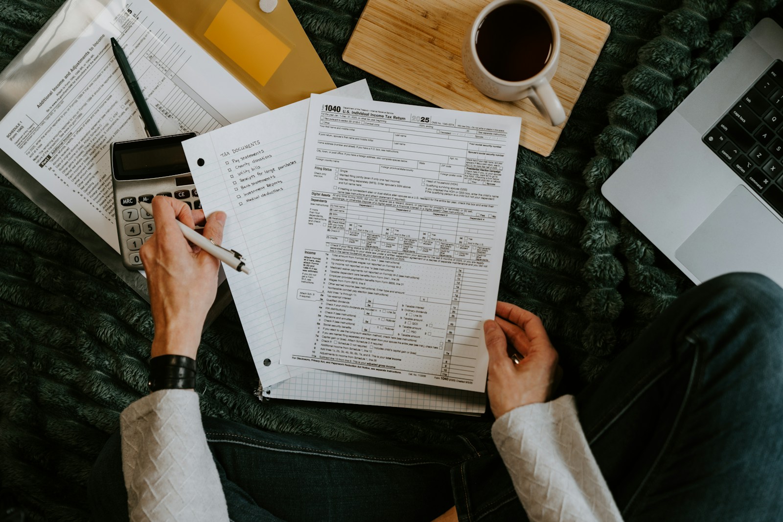 A person reviewing accounting records beside a calculator and laptop