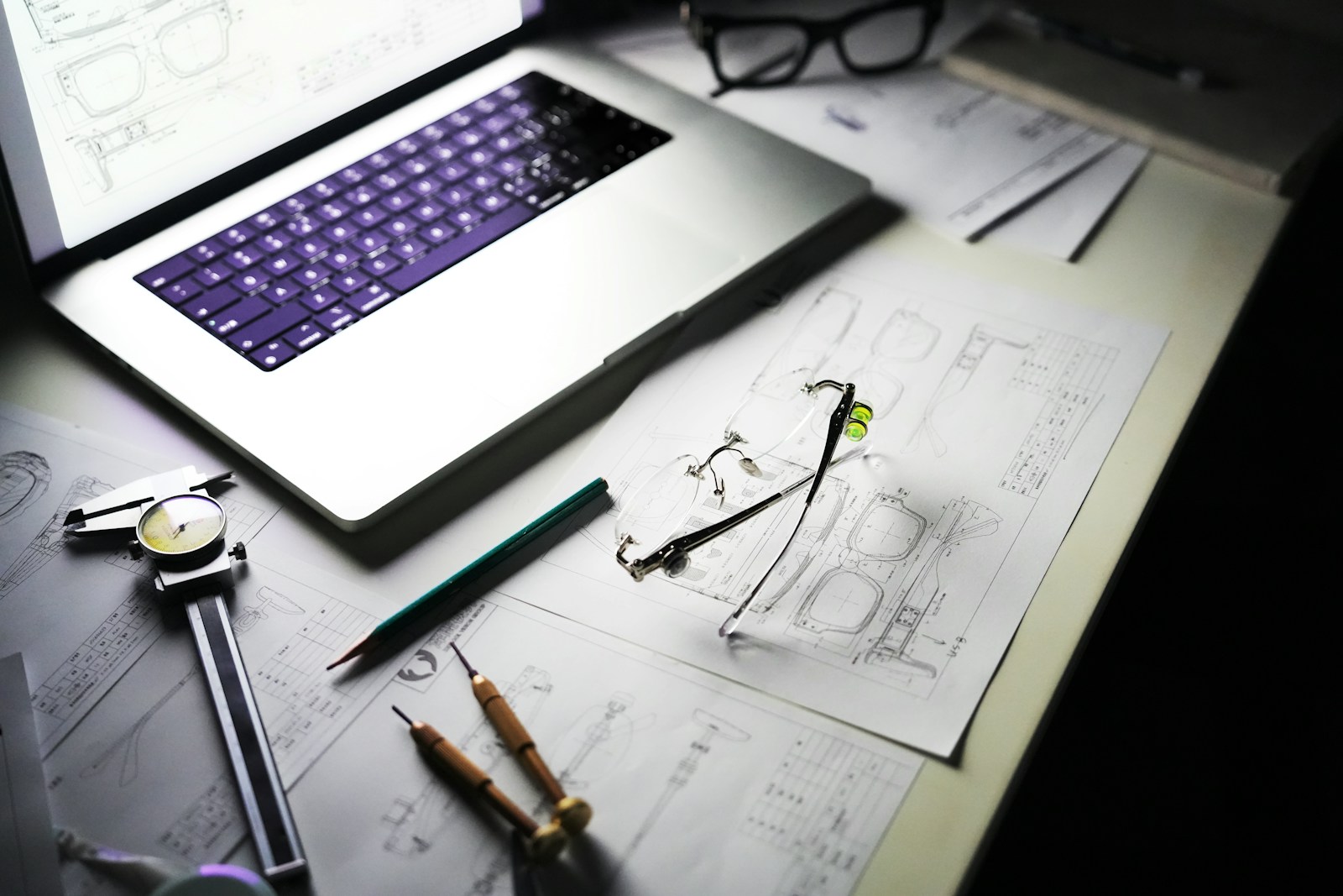 Technical drawings, measuring tools, and a laptop on a design desk